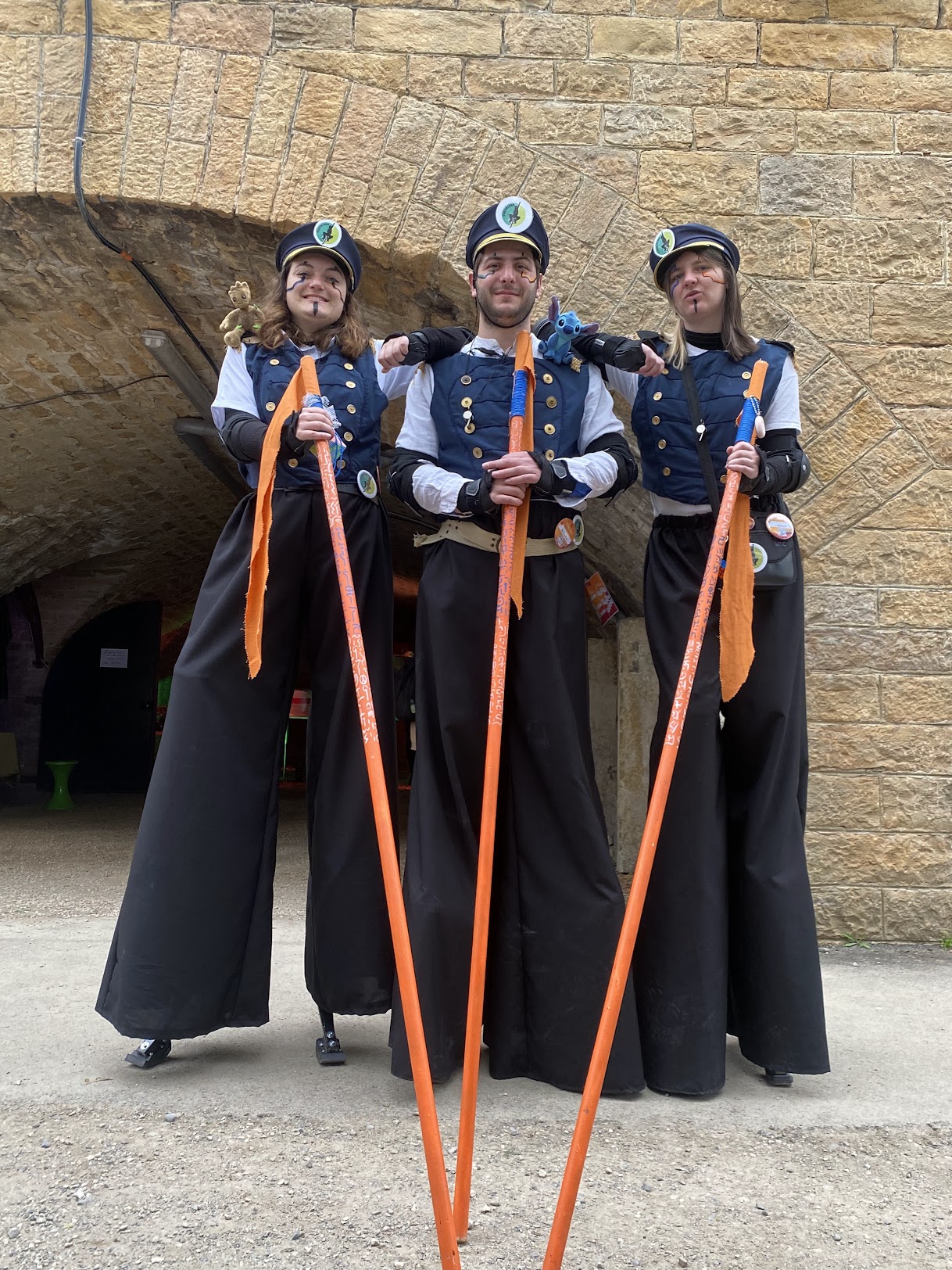 Trois échassiers Yggdriser en costume steampunk d'officier devant une arche en pierre